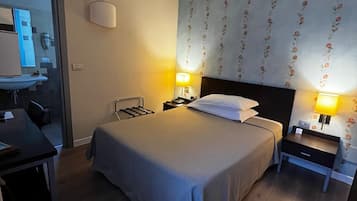 Ein Hotelzimmer mit Bett, Nachttischen, Schreibtisch und einem durchgehenden Türrahmen sichtbarem Badezimmer.