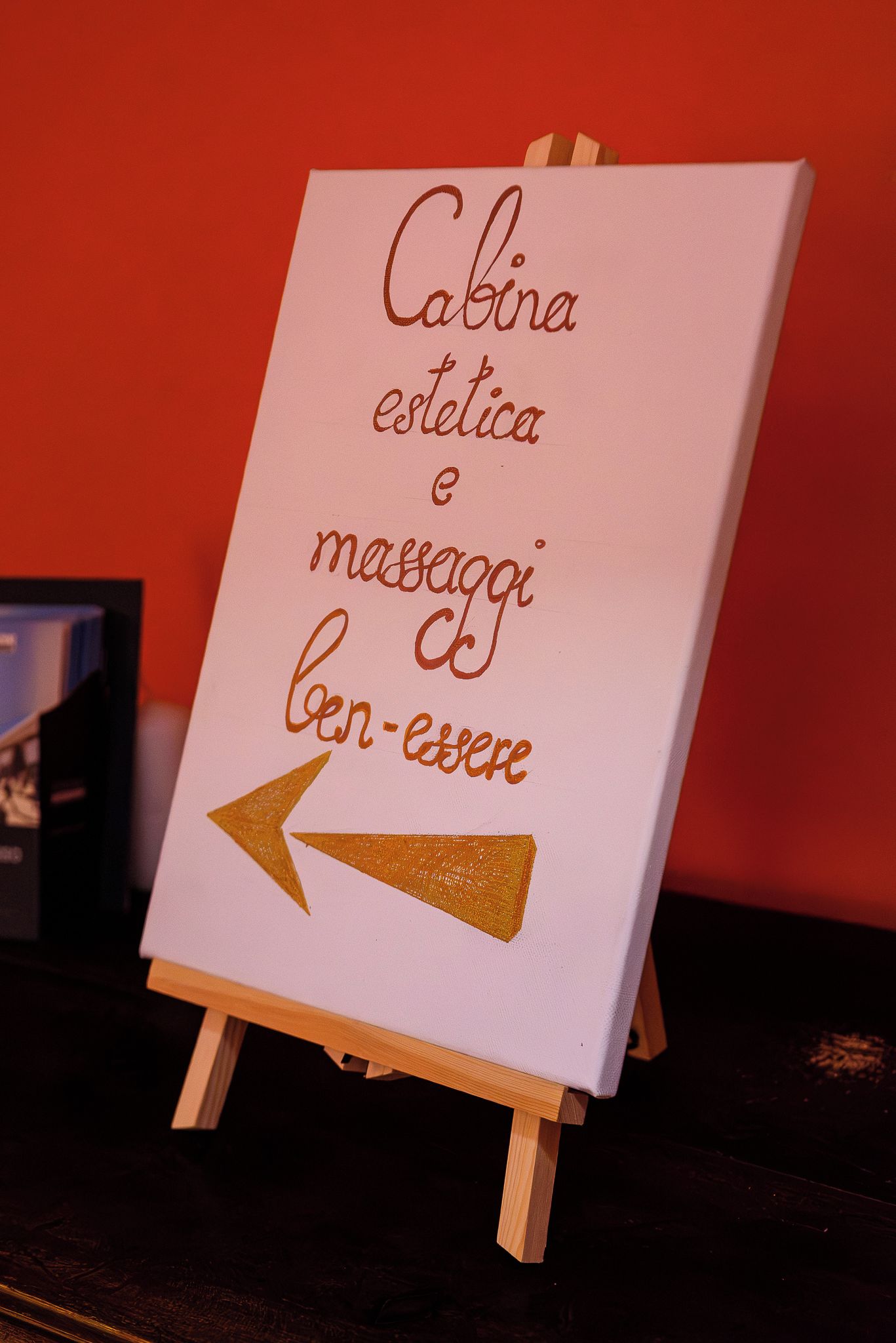 A small easel with a sign that reads 'Cabina estetica & massaggi ben-esere' with an arrow pointing to the left.