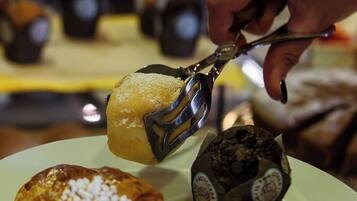 A person holding a pastry with a fork, a croissant, and a chocolate muffin on a plate.