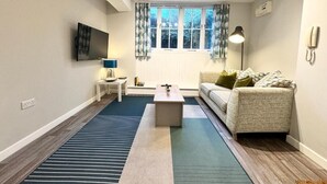 A living room with a flat-screen TV, a sofa, a coffee table, and a window with curtains. - Warehouse Apartments (Ulverston)