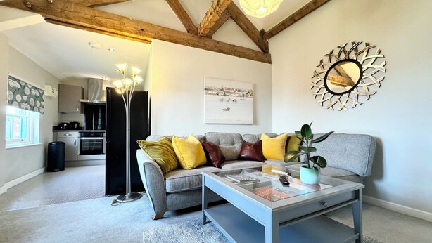 A modern living room with a grey sofa, a coffee table, and a decorative mirror. A kitchen is visible in the background. - Warehouse Apartments (Ulverston)