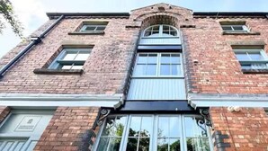 A two-story brick building with a central entrance, large windows, and a flat roof. - Warehouse Apartments (Ulverston)