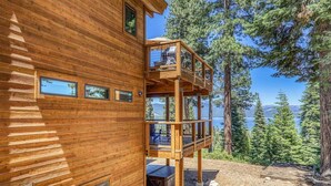 A wooden cabin with a balcony overlooking a forested area and a lake.