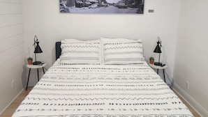A bedroom with a patterned bedspread, two bedside tables with lamps, and a cityscape photograph on the wall. - Cozy Nook Cottage With Hot Tub (Nevada)