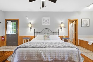 Une chambre à coucher avec un grand lit, deux tables de chevet, un ventilateur de plafond et des œuvres d’art accrochées aux murs.