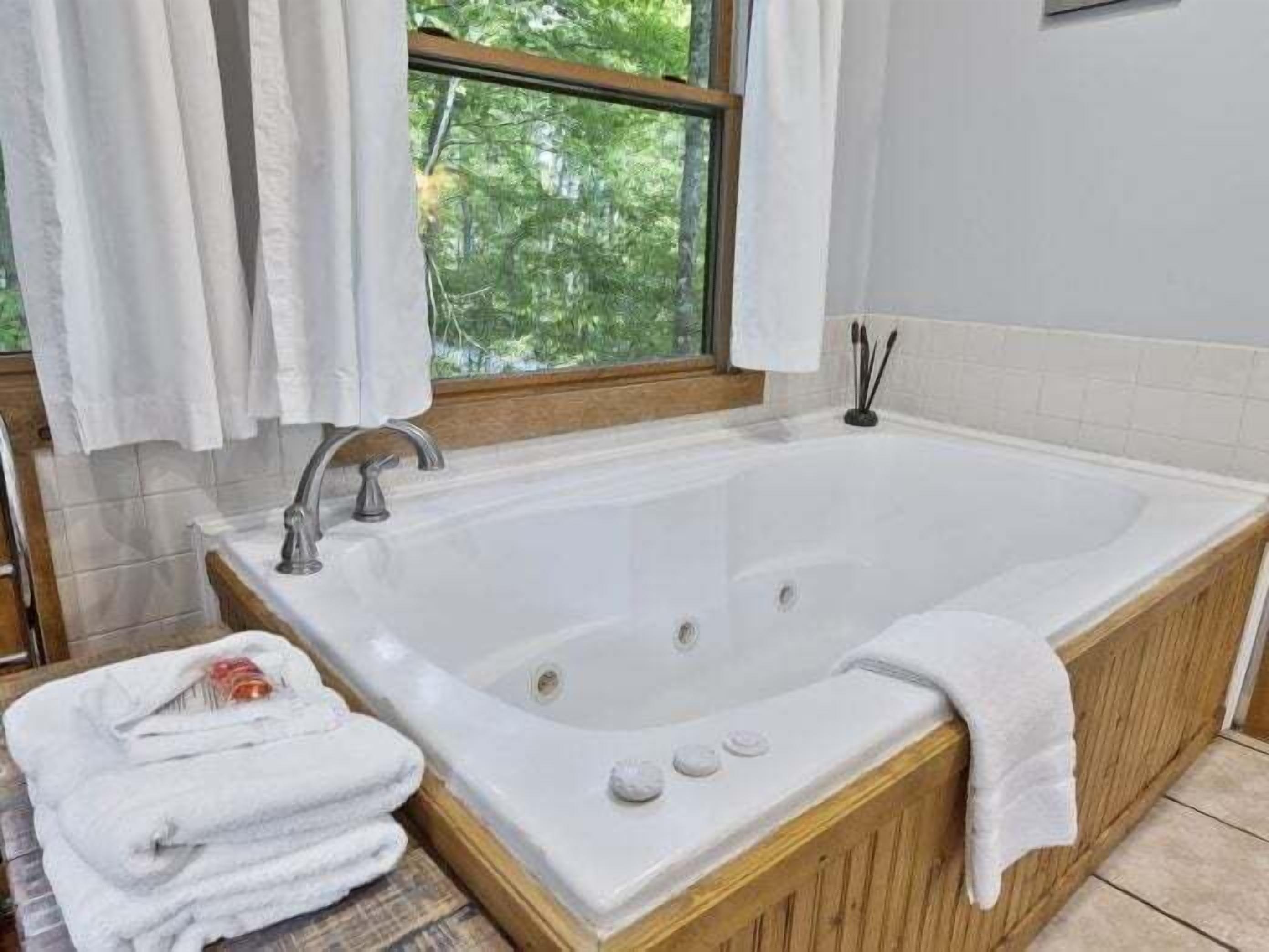 Un baño con una bañera grande, una ventana con cortinas y un perchero para toallas.