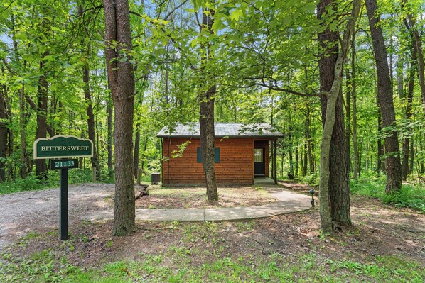 A small wooden cabin labeled 'BITTERSWEET' with a number '21133' in a forested area.