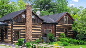 A log cabin with a chimney, wooden exterior, and a garden in front.