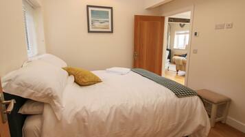 A bedroom with a bed, a bedside table, a mirror, and a door leading to another room.