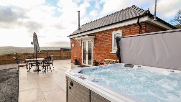 Un jacuzzi en un área exterior cubierta, con una casa de ladrillo al fondo.