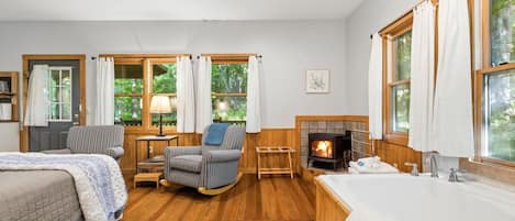 Una habitación acogedora con una cama, un sillón mecededor, una chimenea y un ventanal grande.