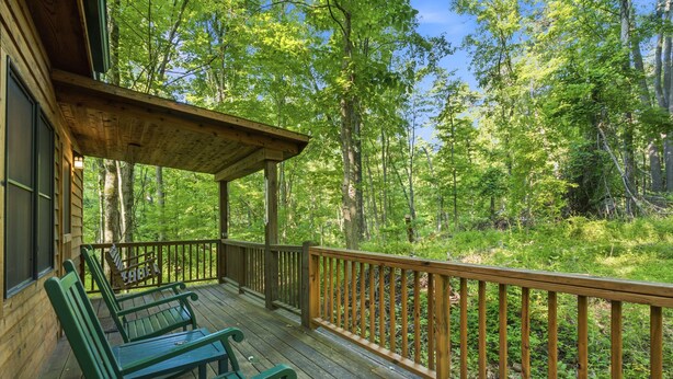 A wooden deck with green chairs and a wooden railing overlooking a forest.