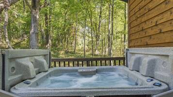A hot tub with a wooden deck and a forest backdrop.