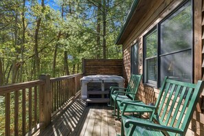 A wooden deck with a stone fireplace, green chairs, and a wooden railing overlooking a forest. - Sumac: ADA-Accessible Hocking Hills Cottage with Outdoor Hot Tub & Breakfast (Logan)
