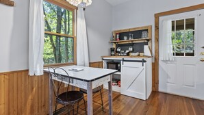 Una cocina compacta con una mesa de madera, una silla, una lámpara colgante y una puerta con ventanal.