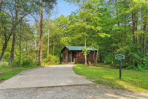 A wooden cabin with a green roof, surrounded by dense forest, accessible via a gravel path. - Sumac: ADA-Accessible Hocking Hills Cottage with Outdoor Hot Tub & Breakfast (Logan)
