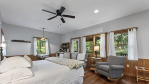 Un dormitorio amplio con una cama grande, un ventilador de techo, un escritorio con silla y una ventana con cortinas.