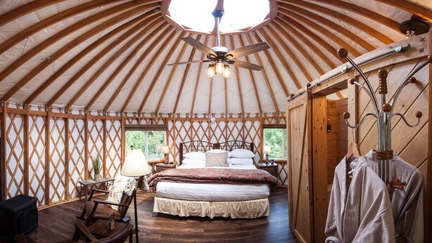 A yurt with a bed, a ceiling fan, and a wooden floor.