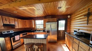 A spacious kitchen with wooden cabinets, a large island, and a stainless steel refrigerator. - VTG Lodge  and Guest Suites - Experience the wild frontier of Crockett Texas (crockett)