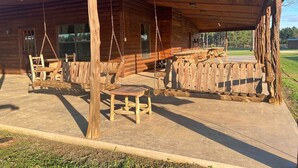 A wooden cabin with a covered patio area featuring a swing set and a table. - VTG Lodge  and Guest Suites - Experience the wild frontier of Crockett Texas (crockett)