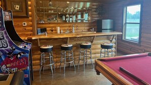 A bar area with stools, a pool table, and a game machine. - VTG Lodge  and Guest Suites - Experience the wild frontier of Crockett Texas (crockett)