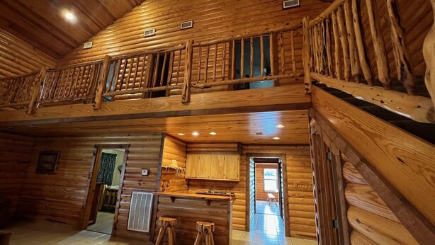 A log cabin interior with a kitchen area, a dining table with stools, and a balcony. - VTG Lodge  and Guest Suites - Experience the wild frontier of Crockett Texas (crockett)
