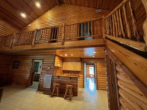 Ein Blockhaus-Interieur mit Küchenzeile, einem Esstisch mit Hocker und einem Balkon.