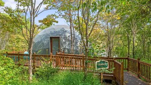 A wooden deck leading to a dome-shaped structure labeled "Petridot" in a forested area. - Peridot Geodome: Wooded Hocking Hills Retreat with King Bed, Private Deck and Breakfast (Logan)