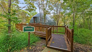A wooden bridge leading to a geodesic dome structure labeled "PERIOD." - Peridot Geodome: Wooded Hocking Hills Retreat with King Bed, Private Deck and Breakfast (Logan)