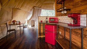 Une cuisine compacte avec un réfrigérateur rouge, un four à micro-ondes et une machine à café. On y trouve une table à manger avec des chaises et une fenêtre avec des rideaux.