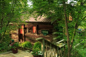A rustic wooden cabin with a porch, surrounded by lush greenery.