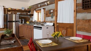 A rustic kitchen with wooden walls, a stainless steel refrigerator, a white stove, and a dining table set with plates and wine glasses. - Tree House: Romantic Hocking Hills Cabin with King Bed, Soaking Tub and Free Breakfast (Logan)