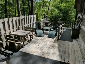 A wooden deck with picnic tables and chairs, surrounded by a wooden fence, set in a forested area. - Pine Grove: Dog-Friendly Hocking Hills Log Cabin with 2 Queen Bedrooms and Free Breakfast (Logan)