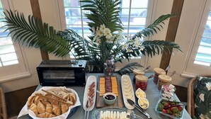 Un buffet de petit-déjeuner avec des croissants, du fromage, de la charcuterie et des fruits, disposés sur une table agrémentée d’un grille-pain et d’un vase de fleurs.