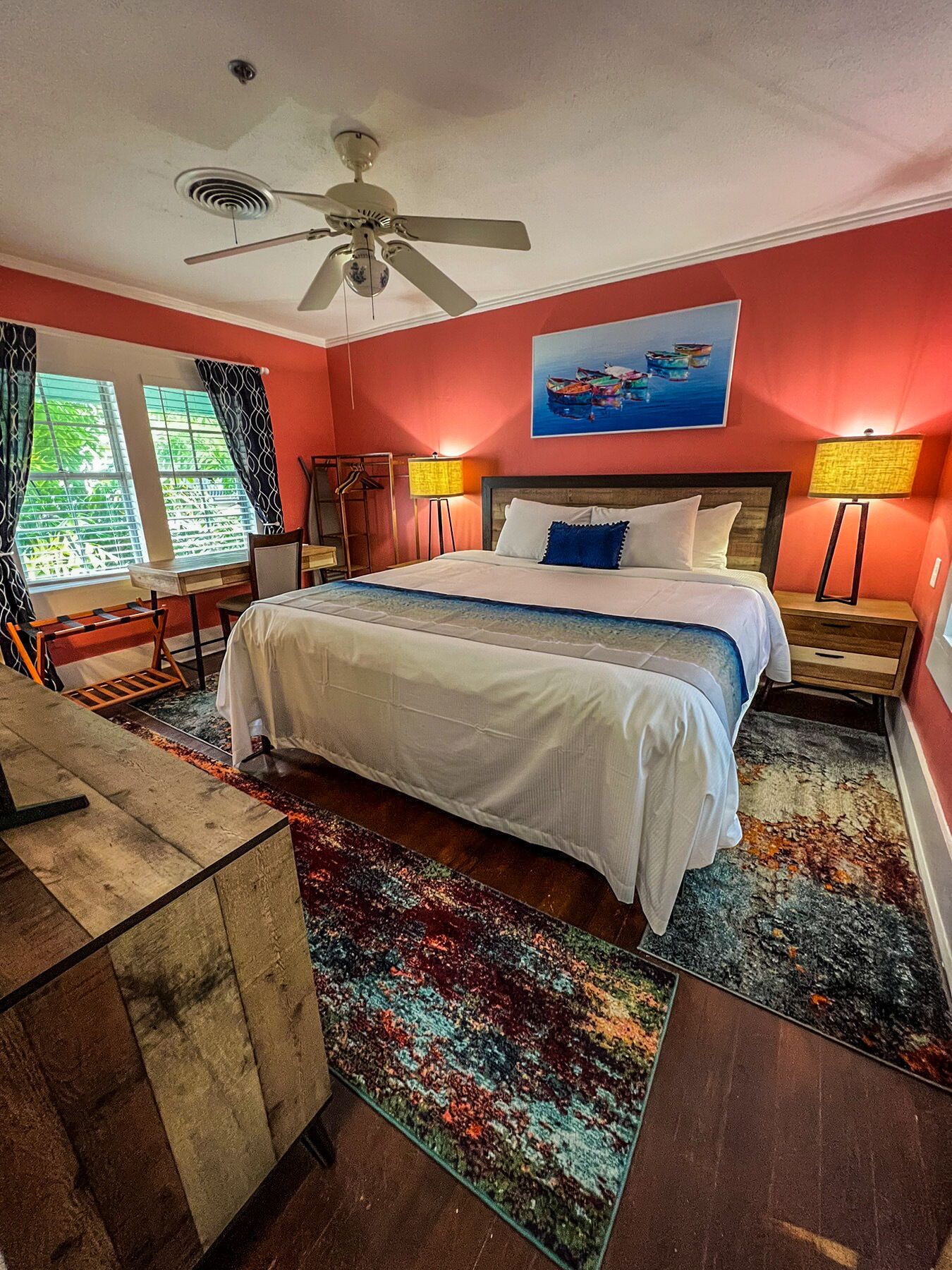 A hotel room with a large bed, two bedside lamps, a ceiling fan, a desk, and a chair.