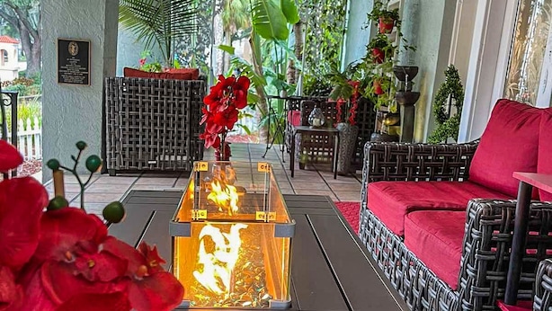Un espace extérieur aménagé avec une zone salon couverte, dotée de meubles en osier, d’une table centrale ornée d’une bougie allumée et d’une végétation luxuriante en arrière-plan.