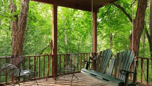 Eine Holzterrasse mit Schaukelstuhl und Bank, umgeben von Bäumen.
