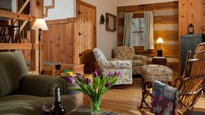Ein gemütliches Wohnzimmer mit Holzmöbeln, einer Treppe und einer Vase mit violetten Blumen.