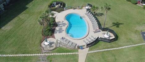 Vue aérienne d’un hôtel doté d’une piscine centrale, entourée de chaises longues et de palmiers.