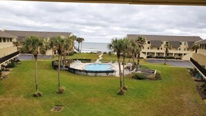 A pool area with palm trees, a view of the ocean, and a building with multiple floors. - Summerhouse 433 (St. Augustine)