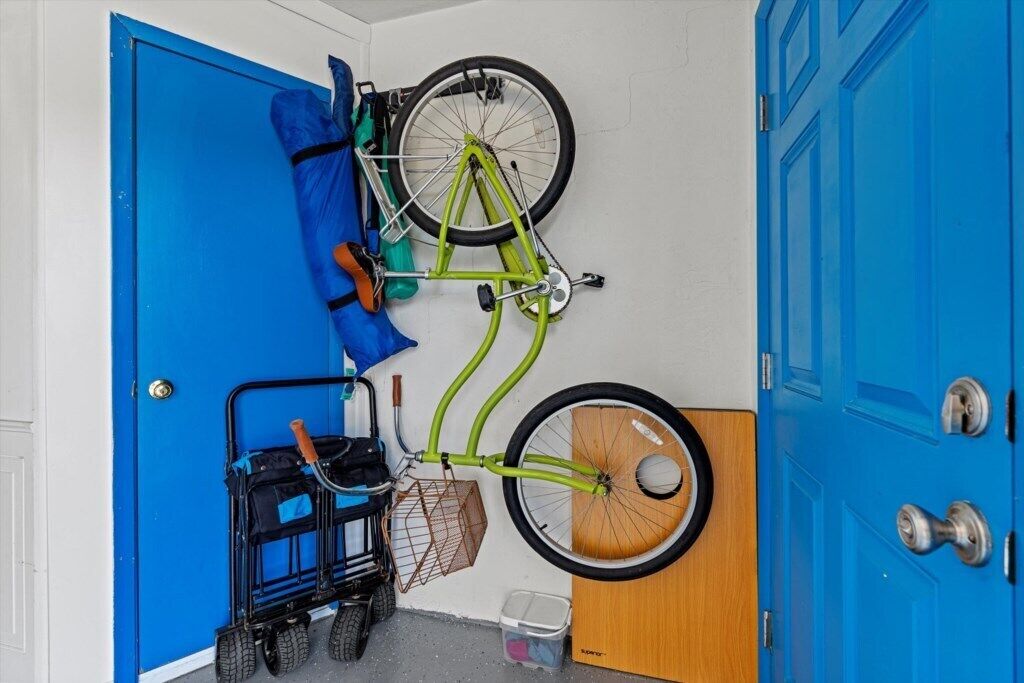 Une pièce avec une porte bleue, un vélo vert accroché au mur, un chariot à bagages noir et une porte en bois.