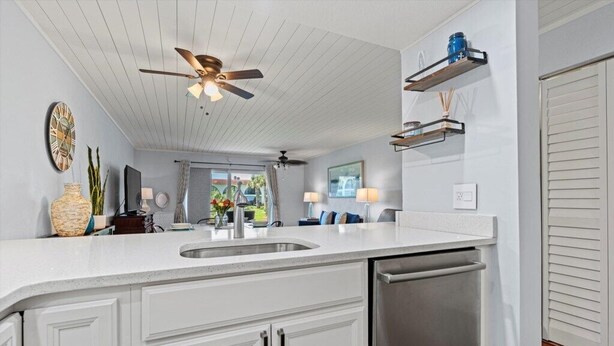 A modern kitchen with white cabinetry, a stainless steel dishwasher, and a ceiling fan. - Ocean Club 37 (St. Augustine)