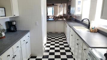Cozinha com armários brancos, chão quadriculado em preto e branco e uma janela que oferece luz natural.