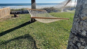 A hammock tied between two trees on a grassy area with a view of the ocean. - Coastal Bliss (St. Augustine)