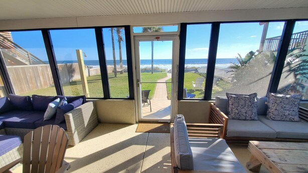 A sunlit room with large windows, a wooden bench, and a cushioned seating area. - Coastal Bliss (St. Augustine)