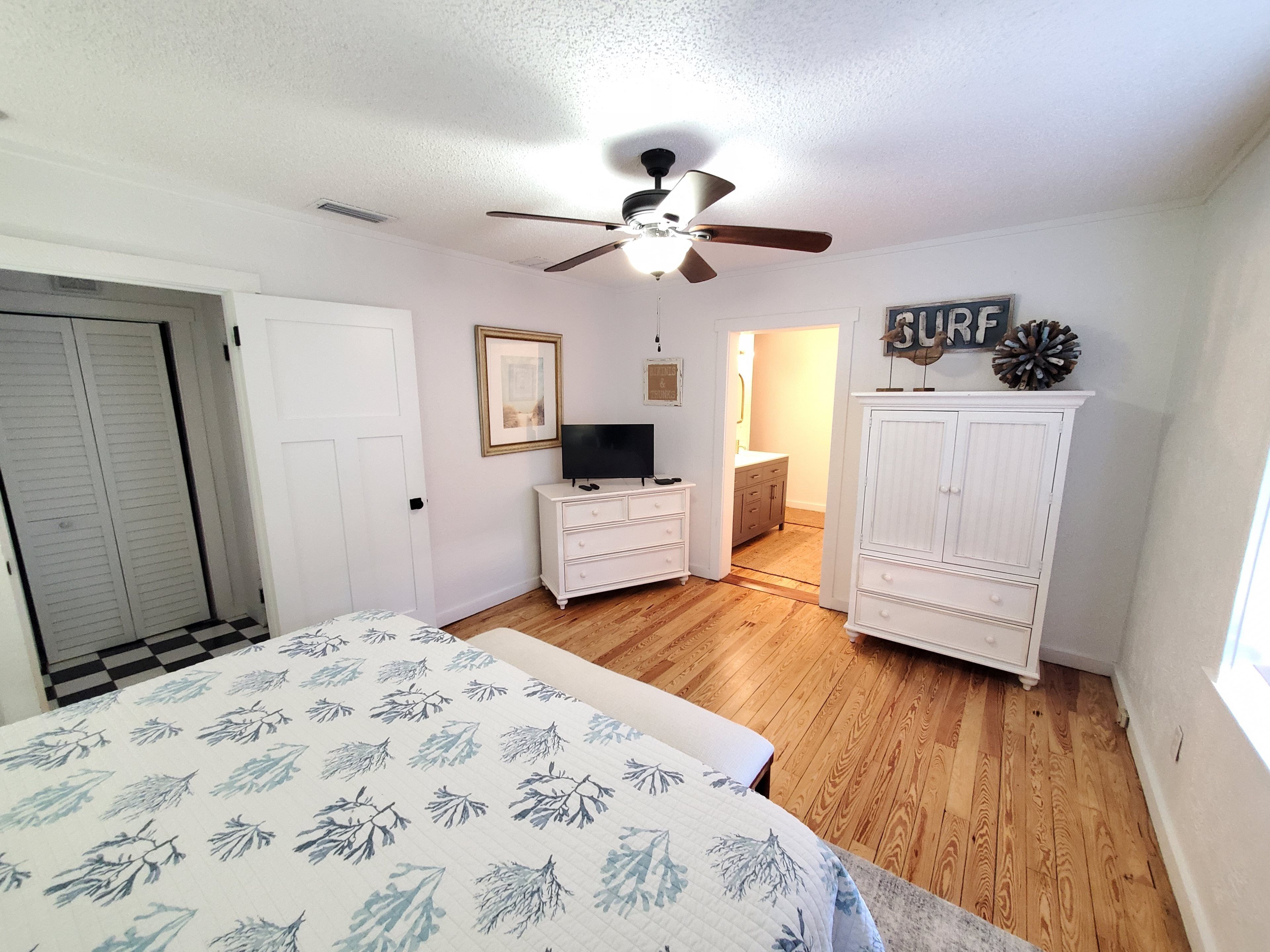 A bedroom with a bed, a ceiling fan, a dresser, a TV, and a wardrobe.