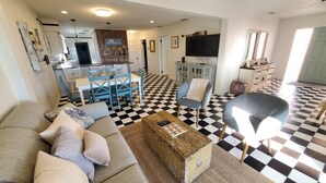 A living room with a checkered floor, a sofa, a coffee table, and a dining area with blue chairs and a white table. - Coastal Bliss (St. Augustine)