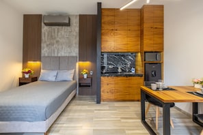 A modern hotel room with a bed, bedside tables with lamps, a wooden kitchenette, and a dining area. - El Desierto by Naya Homes (San José del Cabo)