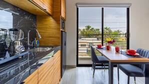 A modern kitchen with a marble countertop, wooden cabinets, and a dining area with a table and chairs. - El Desierto by Naya Homes (San José del Cabo)