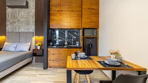 A modern room with a bed, a wooden dining table, a kitchen area, and a built-in TV. - El Desierto by Naya Homes (San José del Cabo)